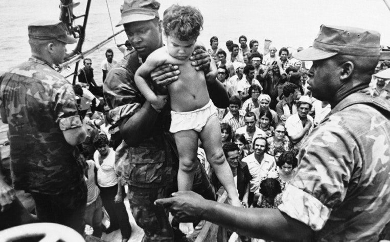 A U.S. Marine carries a child off a boat in Key West. May 1980. (FERNANDO YOVERA / AP)